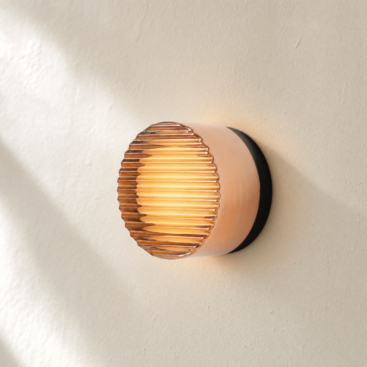 Ansa wall sconce in Amber Stripe art glass, lit on a cream plaster wall